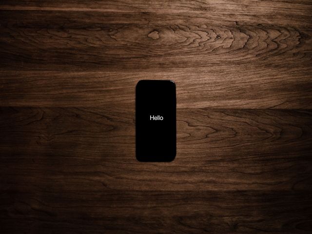 Black iphone screen with the word 'hello' across the screen on a brown table